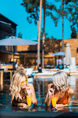 stylish women relaxing in swimming pool with cocktails