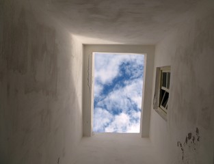 Partly cloudy sky and sunlight seen through the opening in the roof of a traditional Moroccan style building
