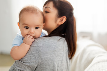 Fototapeta na wymiar family and motherhood concept - close up of happy young asian mother kissing little baby son at home