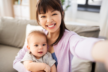 family, parenthood and people concept - happy asian mother with baby son taking selfie at home