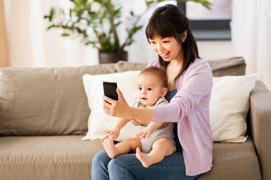 family and motherhood concept - happy smiling young asian mother with little baby son taking selfie by smartphone at home