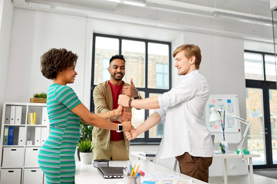 business, teamwork and corporate concept - happy creative team making thumbs up gesture at office