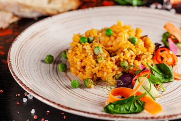 Concept of Spanish cuisine. Paella with seafood and shrimps, with green peas in a clay plate. A glass of cool wine is on the table. background image, copy space