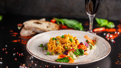Concept of Spanish cuisine. Paella with seafood and shrimps, with green peas in a clay plate. A glass of cool wine is on the table. background image, copy space