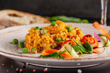 Concept of Spanish cuisine. Paella with seafood and shrimps, with green peas in a clay plate. A glass of cool wine is on the table. background image, copy space