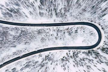 Curvy windy road in snow covered forest, top down aerial view. Winter landscape.