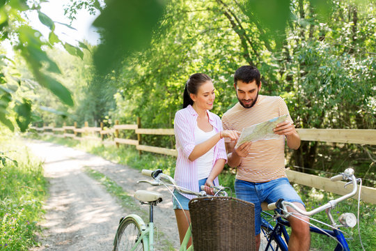 travel, trip, leisure and lifestyle concept - happy young couple with map and bicycles looking for location at country in summer - Powered by Adobe