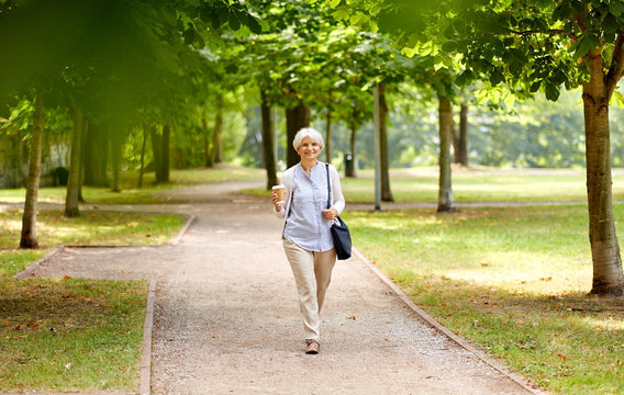 old age, retirement and people concept - close up of happy senior woman walking with takeaway coffee cup along summer park