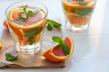 glasses with a refreshing drink with orange and mint leaves on a napkin on a blonded background.