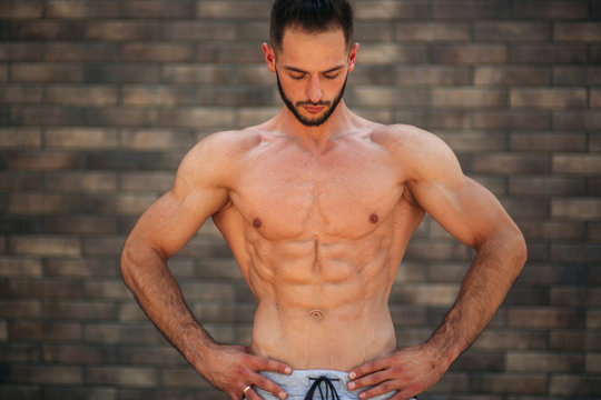 Young athlete posing with a torso for photography on a brick wall background. Bodybuilder, athlete with pumped muscles, breast and arm rescue