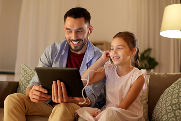 Fototapeta premium family, fatherhood and technology concept - happy father and little daughter with tablet pc computer and earphones listening to music at home in evening