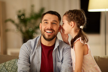 family, fatherhood, leisure and people concept - happy daughter whispering secret to father at home...