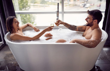 Smiling man and woman have fun together in the bathtub and drinking champagne.