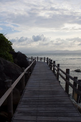 Obraz premium Wooden board bridge around cliff cape with cloudy sky above the sea