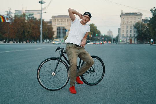 Portrait of young man walking with thoughtfully classic bicycle on city streets