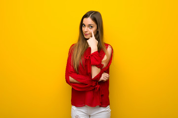 Young girl with red dress over yellow wall looking to the front