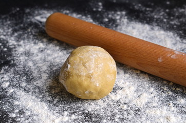 Ball of dough and wooden rolling pin on dark floured surface