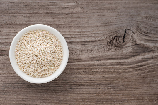 Sesame seeds in a small white bowl on a wooden background.
