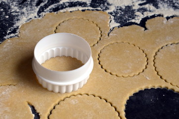 White cookie cutter on rolled out pastry on dark floured counter