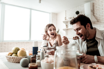 Bearded handsome positive man in a white shirt eating having breakfast with his wife