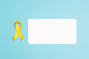 Childhood Cancer Awareness Yellow Ribbon with blank paper card for text on blue background.