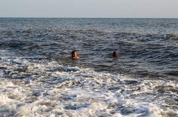 A man and a boy teenager swim in the sea, on big waves
