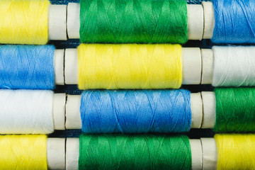 Spools of blue, yellow, green and white  sewing thread arranged in rows on denim