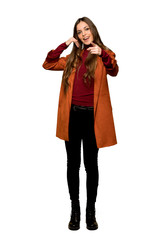 Full-length shot of Young woman with coat making phone gesture and pointing front on isolated white background