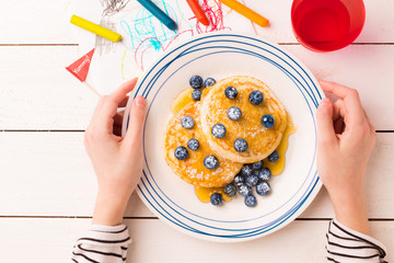Breakfast in child's hands - pancakes, blueberries and maple syrup