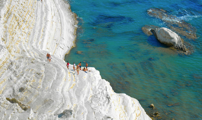 white cliffs naturally made of smooth pug at Scala dei Turchi beach full of people with turquoise mediterranean sea and blue cloudy summer sky near Agrigento, Sicily, Italy
