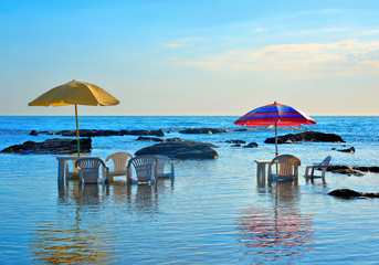 chair and table immersed in water, umbrella with the background of a colorful warm summer sunset and beautiful water reflections, Agrigento Italy