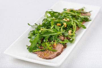 appetizer of baked meat with sauce and fresh herbs, arugula, spices on white plate. Close up