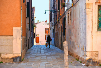 Fototapeta na wymiar a glimpse of Venice with woman in the very narrow street in the middle of the old red brick houses overlooking a canal in Venice Italy