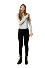 Full-length shot of young girl surprised and pointing side on isolated white background