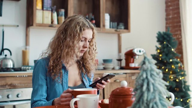Girl typing a message in the smartphone in the morning in the kitchen
