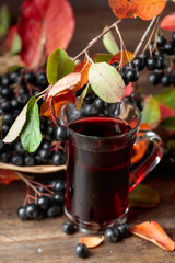 Fresh juice of ripe black chokeberry in glass and berries with leaves.
