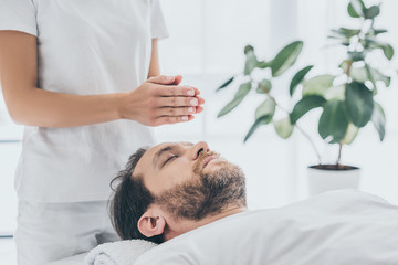 cropped shot of female hands and bearded man receiving reiki treatment