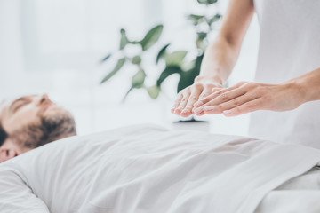 cropped shot of bearded man lying and receiving reiki treatment on stomach