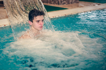 Young man having fun with the water in the swimming pool. Happy young man having fun and relaxing under a water jet at swimming pool