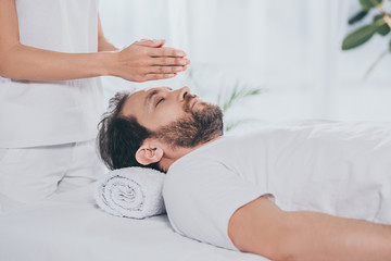 cropped shot of bearded man with closed eyes receiving reiki treatment above head