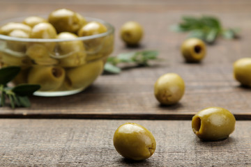 Green olives with leaves in a glass bowl on a brown wooden table. close-up