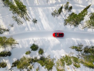 Aerial view of red car driving through the white snow winter forest on country road in Finland,...