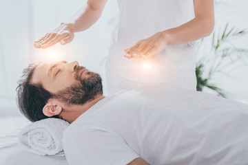 cropped shot of bearded man with closed eyes receiving reiki healing treatment