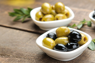 Green and black olives with leaves in a white bowl on a brown wooden table. close-up