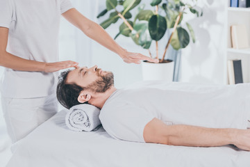 cropped shot of reiki healer doing treatment session to calm bearded man with closed eyes