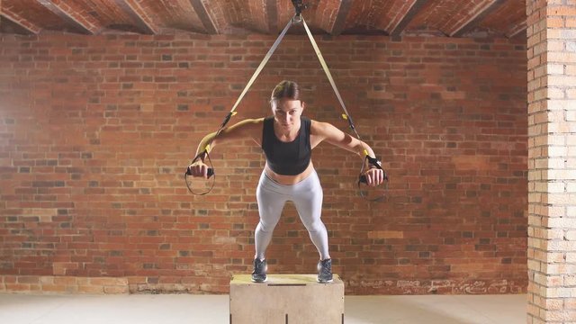 Athletic girl is engaged in crossfire. A young athlete is engaged with a trx in the gym.
