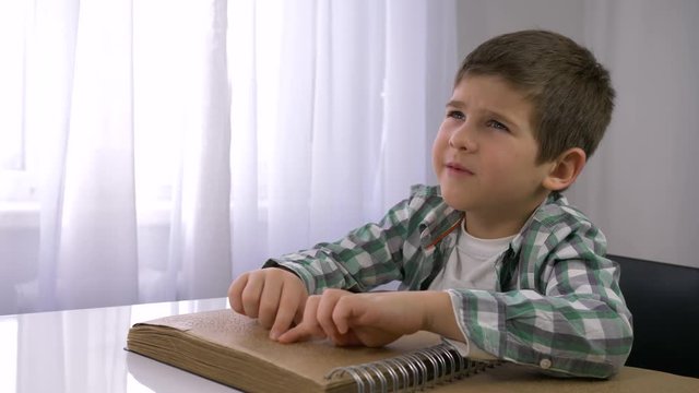 blind child boy reading braille book with symbols font for Visually impaired sitting at table indoors