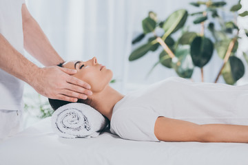 cropped shot of calm young woman with closed eyes receiving reiki healing therapy