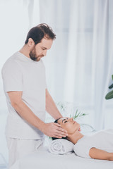 young woman with closed eyes receiving reiki treatment from bearded healer