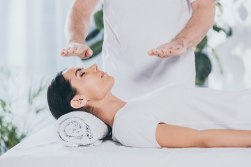 cropped shot of male healer doing reiki treatment session to young woman with closed eyes - obrazy, fototapety, plakaty
